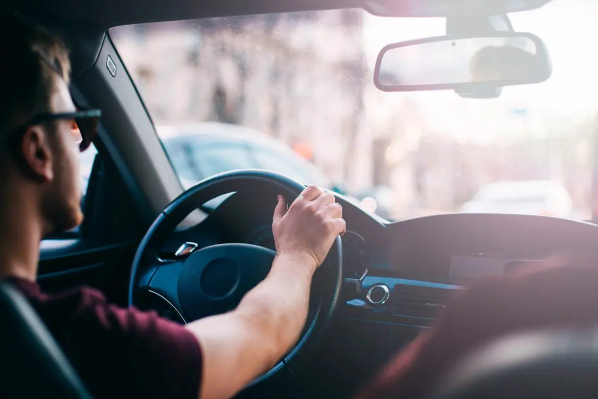 A person is driving in the car while holding on to the steering wheel.